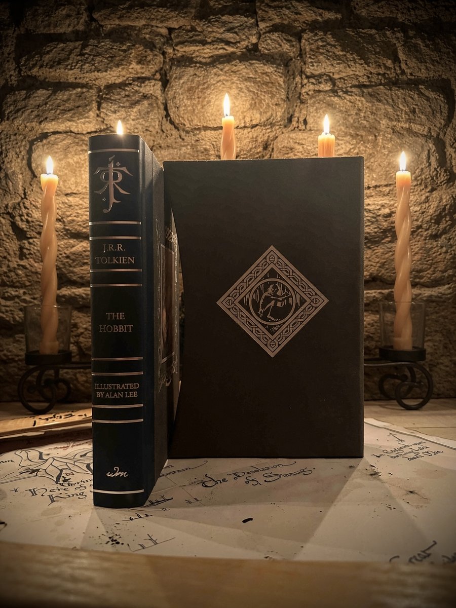 The Hobbit deluxe edition illustrated by Alan Lee standing beside its dark slipcase, lit by candles against a stone wall, on a hand-drawn map